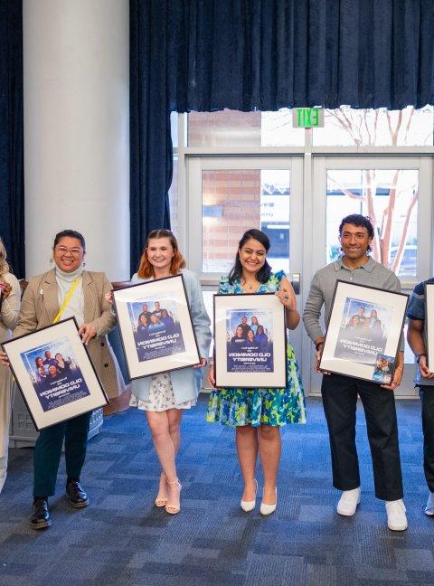 students standing while each holding a framed movie poster 